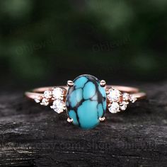 a turquoise ring with white stones on top and gold trim around the band, sitting on a piece of wood