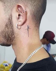 a man's neck with a cross tattoo on the top of his left ear