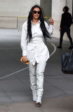 a woman with long black hair and sunglasses walking down the street holding a yellow purse