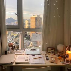 a desk with a laptop computer on top of it next to a window overlooking the city