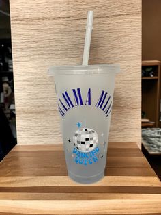 a plastic cup with a straw in it on a wooden table next to a wall