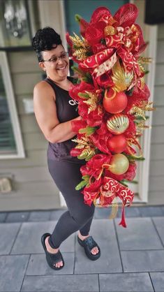 a woman in black top and grey leggings holding up a red christmas tree