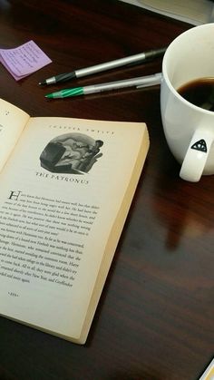 an open book sitting on top of a wooden table next to a cup of coffee