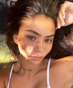 a young woman with freckles on her chest posing for the camera while wearing a white tank top