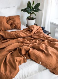 an unmade bed with brown sheets and a potted plant