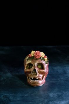 a skull with flowers on its head sitting on a blue surface in front of a black background