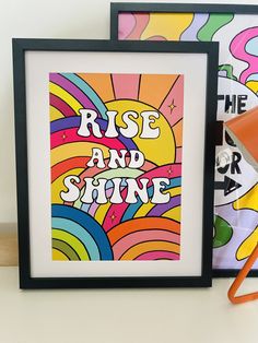 two framed art pieces sitting next to each other on a table with an orange lamp