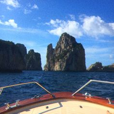 the bow of a boat in front of two large rock formations on the ocean with blue sky and clouds