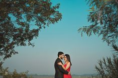 a man and woman standing next to each other in front of trees with the sky behind them