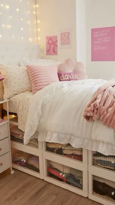 a white bed with pink pillows and blankets in a room filled with drawers underneath the bed