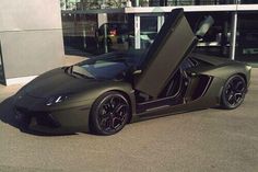 a green sports car parked in front of a building with its doors open and the door opened