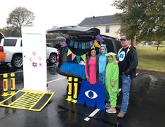 three people standing in front of a car with an eye on it and decorations hanging from the trunk