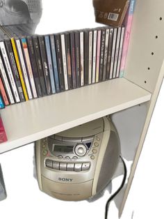 a cd player sitting on top of a white shelf next to a bunch of dvds