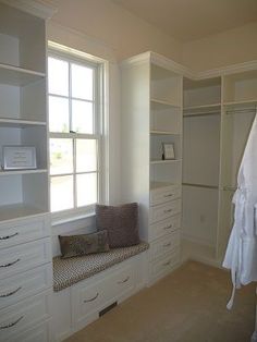 a white closet with drawers, shelves and a bench in front of a window that is open