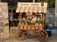 an old fashioned wooden cart with flowers on the side and people standing around in front