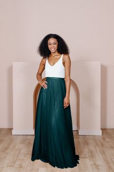 a woman standing in front of a wall wearing a green skirt and white tank top