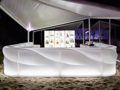 an outdoor bar is lit up at night with white lights on the side and shelves behind it