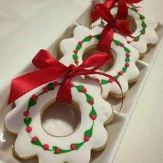 decorated cookies in the shape of christmas wreaths on a white tray with red ribbon