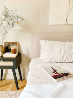 a bed with white sheets and pillows in a bedroom next to a painting on the wall