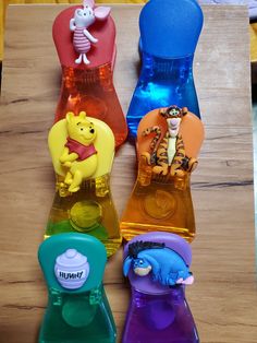 four winnie the pooh bottle stoppers on a wooden table with other plastic items