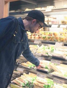 a man looking at food in a grocery store aisle with shelves full of sandwiches and other foods