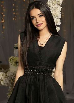 a woman in a black dress posing for a photo with white flowers behind her and lights on the background