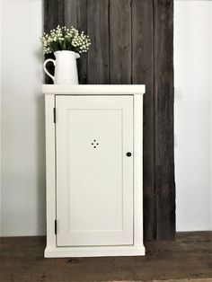 a white cabinet with a vase on top of it next to a wooden wall and floor