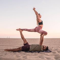 a man and woman doing yoga on the beach with their arms in the air while holding each other's legs