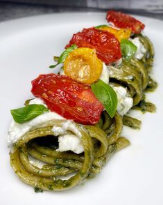 a white plate topped with green pasta covered in sauce and toppings on top of it