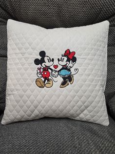 two mickey and minnie mouse pillows sitting on a couch with one holding the other's hand