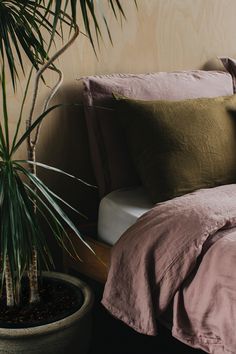 a bed with pink sheets and pillows next to a potted plant