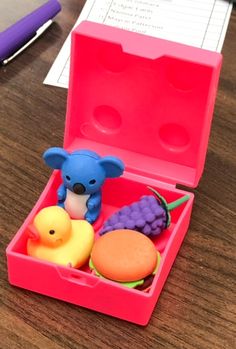 a pink box with some toys in it on a wooden table next to a pen and paper