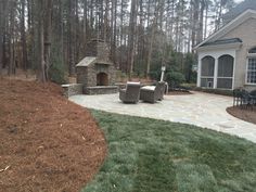 a patio with chairs and a fire place in the middle of it, surrounded by trees