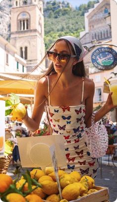 a woman standing in front of a box of lemons and oranges at an outdoor market