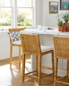 two wicker bar stools in front of a kitchen counter with potted plants