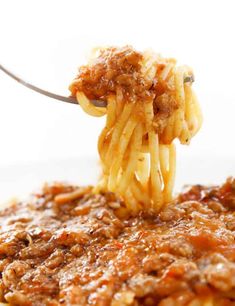 a fork full of pasta with meat and sauce on the top is being held up