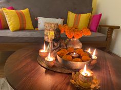 candles are lit on a wooden table in front of a couch with flowers and buddha statues