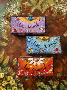 three painted boxes sitting on top of each other in front of some flowers and leaves