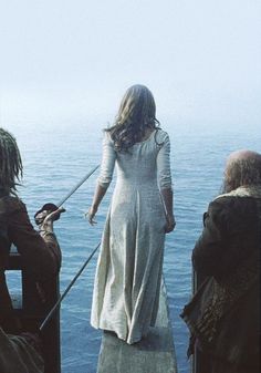 a woman standing on top of a boat next to the ocean while others watch her