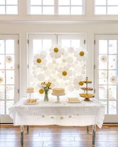 a white table topped with cakes and desserts next to two large windowed windows