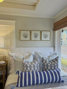 a bed with blue and white pillows on top of it next to a window in a bedroom