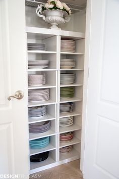 a white bookcase filled with lots of plates and bowls next to a door way