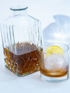 a glass with ice, lemon and water next to a decanter