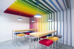 a rainbow colored room with chairs and tables in front of the colorful wall that has vertical stripes painted on it