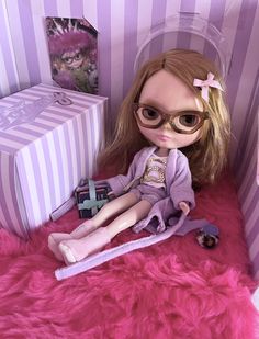 a doll sitting in a pink chair next to a box and some other items on the floor