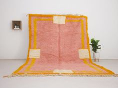 a pink and yellow rug sitting on top of a floor next to a potted plant