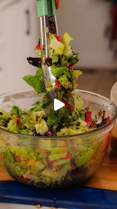 a person using a fork to mix up a salad in a glass bowl on a cutting board