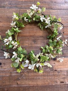 a wreath with white flowers and green leaves on a wooden surface, ready to be used as a decoration