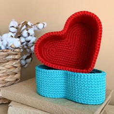 a knitted heart sitting on top of a blue box next to a basket with cotton