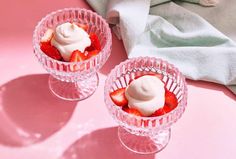 two small glass bowls filled with strawberries and whipped cream on pink table cloth next to white towel